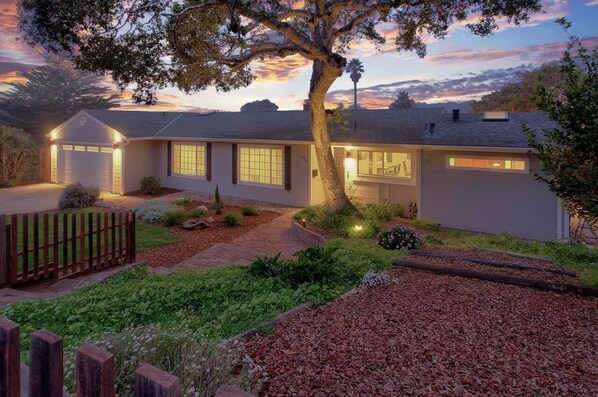 A two-story house with a garage, a well-maintained garden, and a large tree in front.