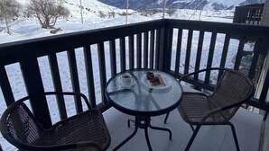 Ein Balkon mit einem Glastisch und zwei Korbstühlen, mit Blick auf eine verschneite Berglandschaft.
