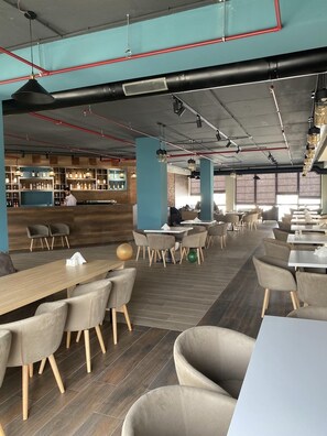 A modern restaurant with a bar area, wooden tables, and chairs.