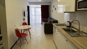 Ein kompakter Wohnraum mit Küchenzeile, einem Essbereich mit roten Stühlen, einer Couch mit Kissen und einem an der Wand montierten Fernseher.