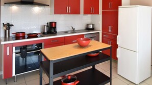 Una cocina compacta con armarios rojos, una estufa negra, un refrigerador blanco y una mesa de madera.