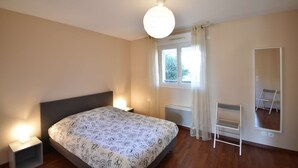 Un dormitorio con cama, mesitas de noche, una ventana con cortinas, un espejo y un radiador.