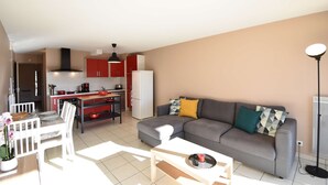 Una sala moderna con un sofá gris, una mesa de comedor y una cocina al fondo.