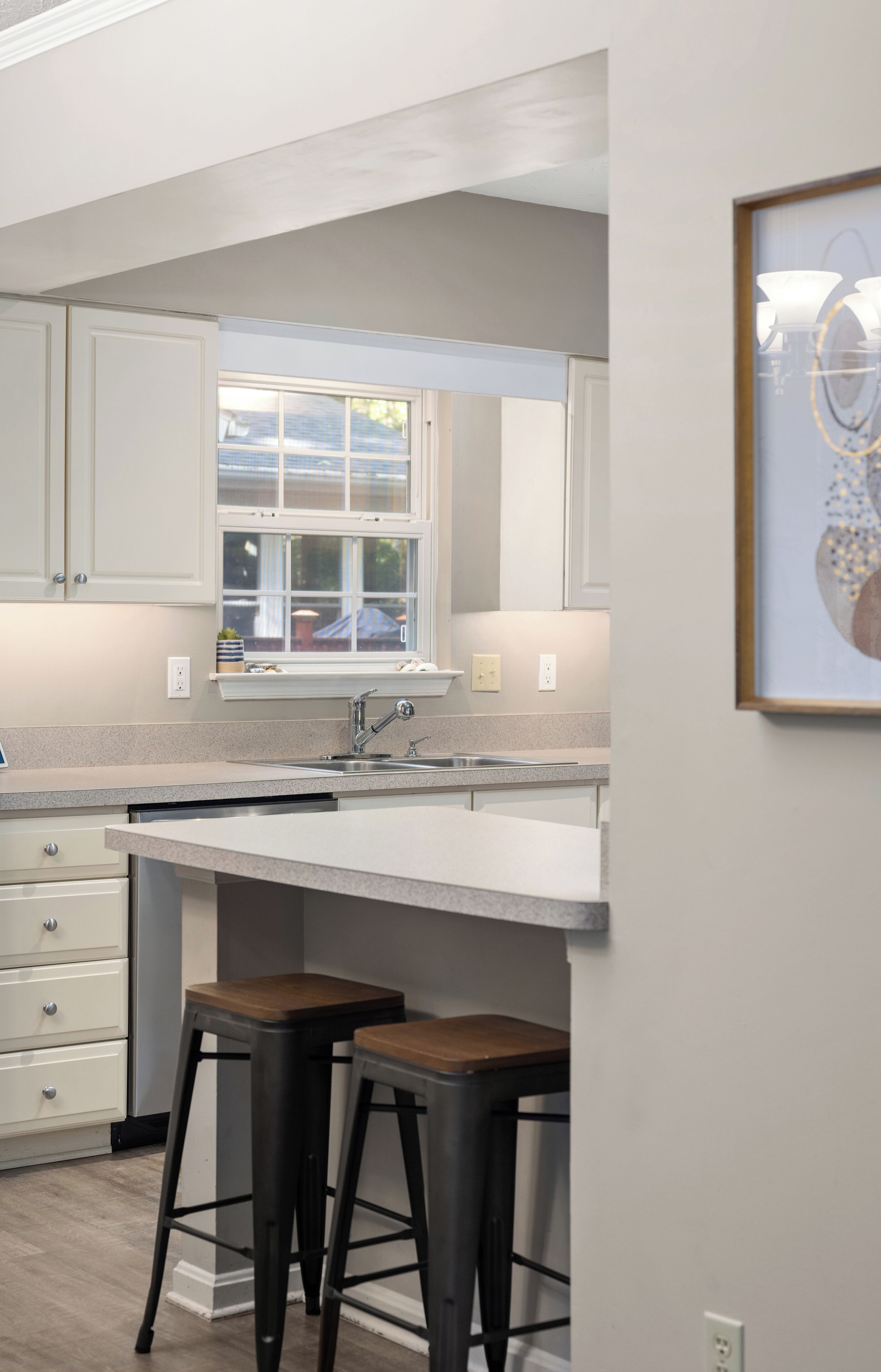 A modern kitchen with white cabinetry, a large window, and two stools.
