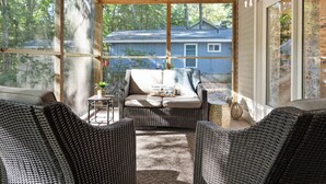 A covered porch with wicker furniture, a ceiling fan, and a view of a house in the background.