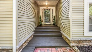 A narrow, symmetrical staircase leading to a front door with a number plate, flanked by two potted plants and a small window on the right.
