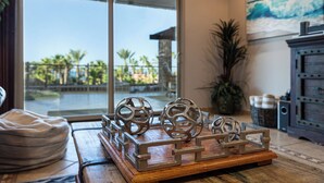 A wooden tray with decorative metal spheres and a metal fence on a table, with a view of palm trees and a building through a large window.