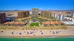 An aerial view of a coastal resort with multiple high-rise buildings, a sandy beach, and clear turquoise waters.