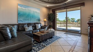 A living room with a leather sofa, a coffee table, a painting, and a view through a glass door.
