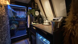 Ett kompakt kök med ett kylskåp, en kaffemaskin och en liten matplats med en växt och ett fönster.