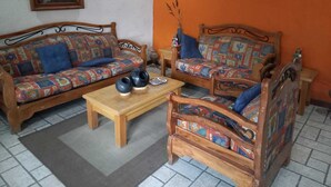 Un salon avec deux canapés en bois recouverts d’un tissu aux couleurs vives, une petite table basse en bois et un tableau accroché au mur.