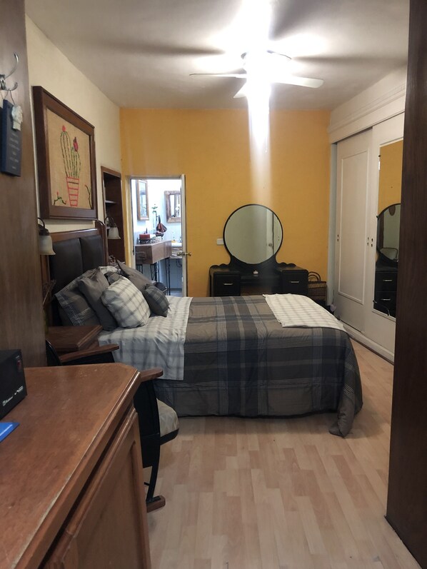 Ein Schlafzimmer mit einem Bett, einem Schreibtisch, einem Schminktisch, einem Spiegel und einer Tür zu einem anderen Raum.