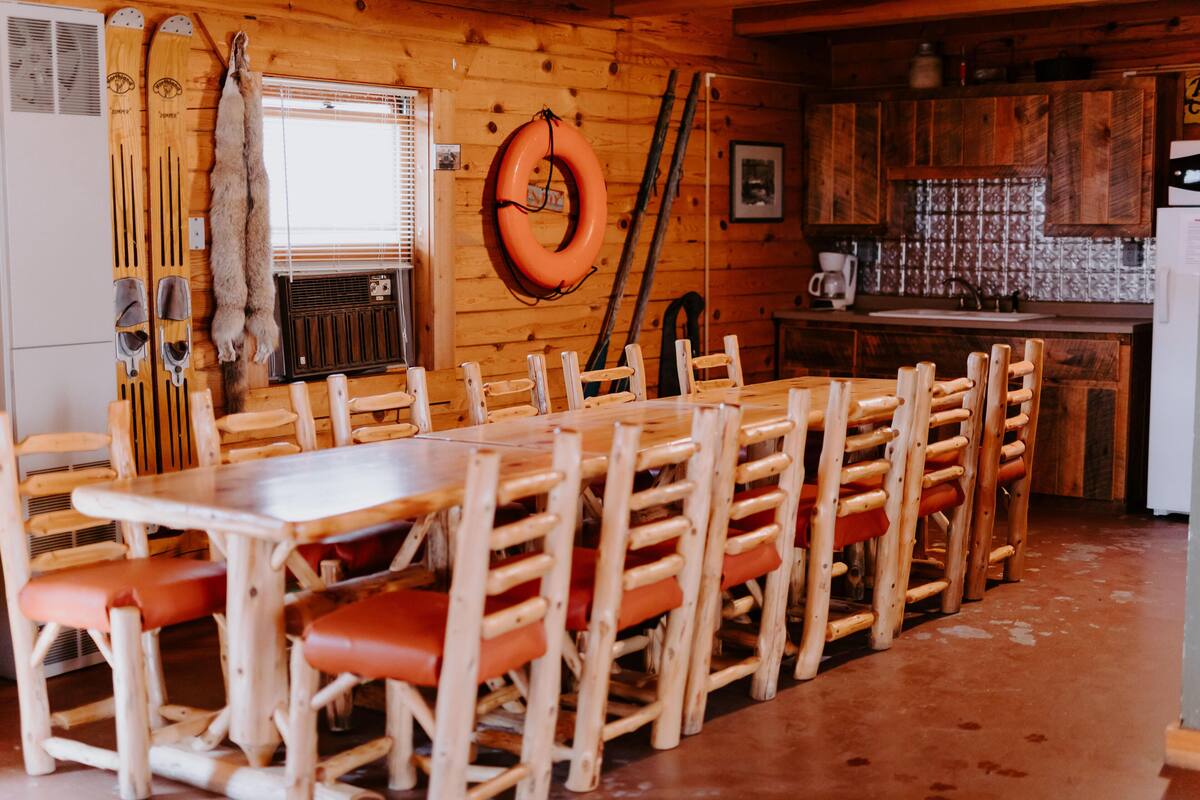 A wooden interior with a dining table and chairs, a kitchen area, and ski equipment.