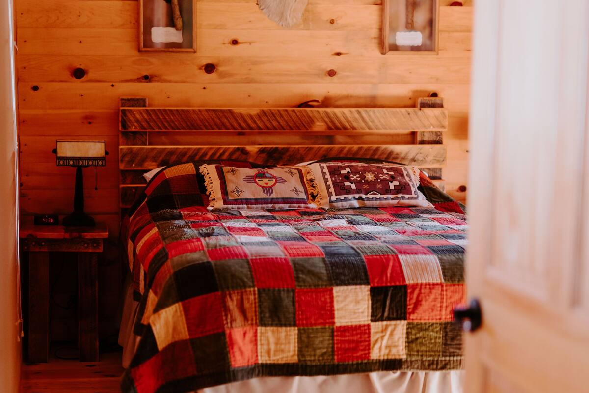 A wooden cabin bedroom with a bed, a wooden headboard, a quilt, and two mounted deer heads on the wall.
