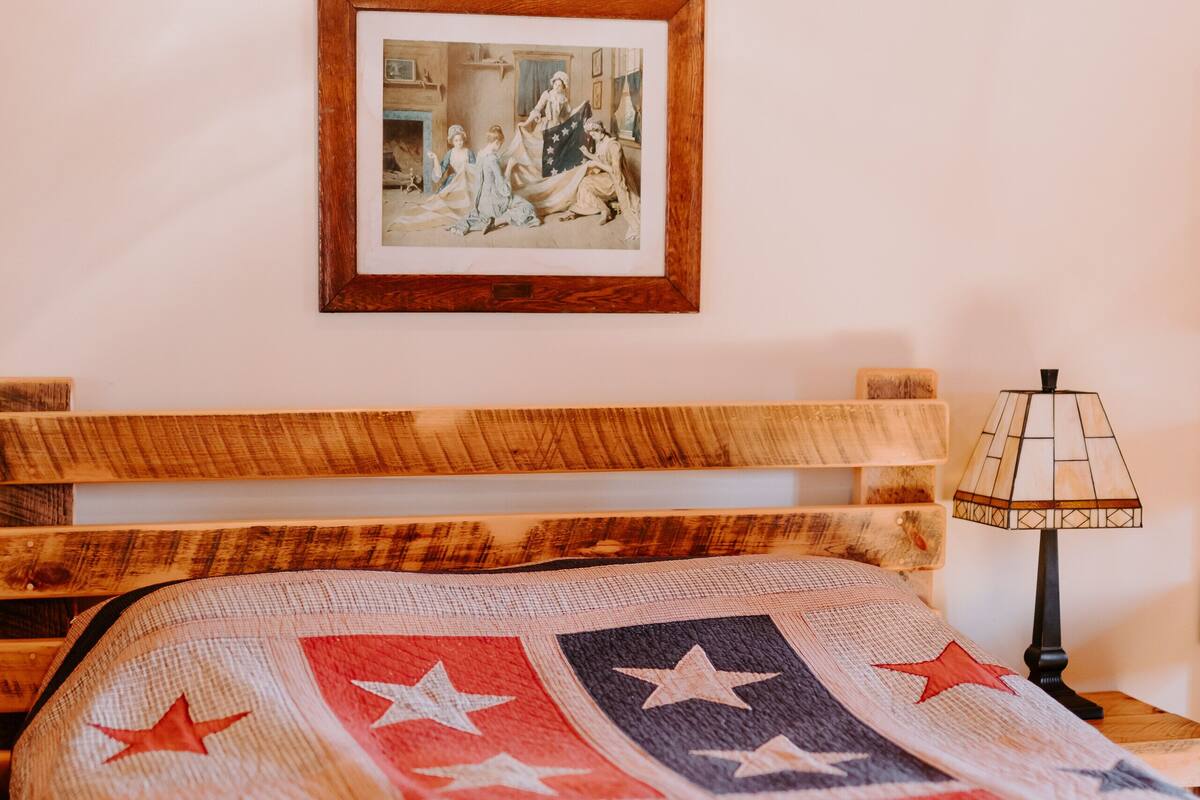 A bed with a quilt featuring stars, a framed picture on the wall, and an American flag.