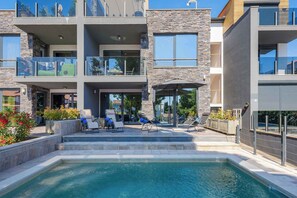 A modern multi-story building with a swimming pool, outdoor seating, and a stone facade. - Holiday apartment with shared pool, air conditioning (Nova Vas/Poreč)