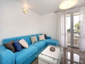 A modern living room with a blue sofa, a glass coffee table, and a ceiling light fixture.