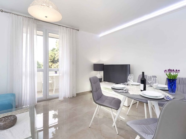 A modern dining area with a flat-screen TV, a dining table set for four, and a sofa in the background.