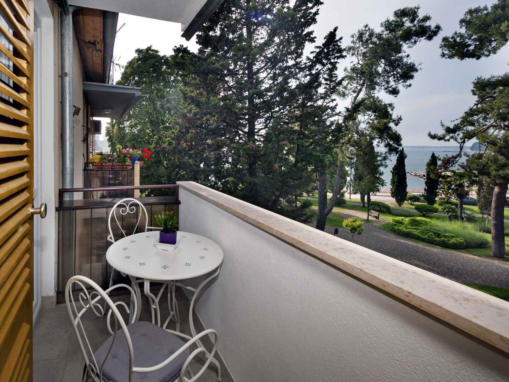 A balcony with a table and chairs, overlooking a landscaped garden and a body of water.