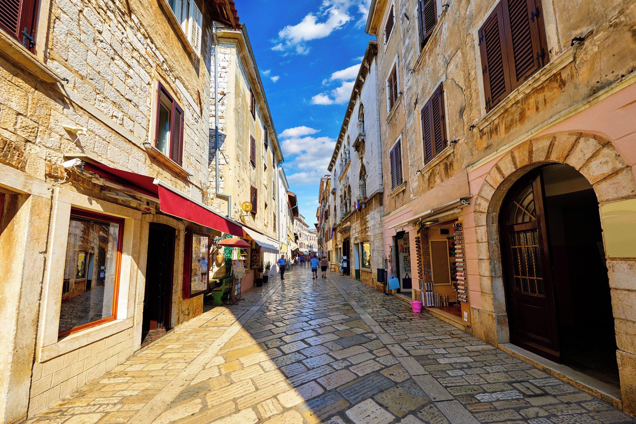 A cobblestone street in a historic town with stone buildings, shops, and a clear blue sky.