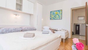 A modern bedroom with a large bed, a small bedside table, a wall-mounted light, and a painting.