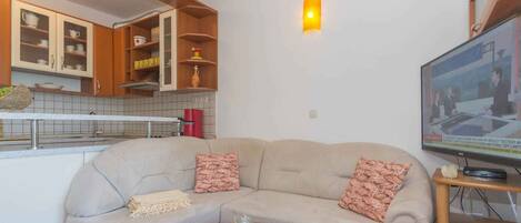 Een woonkamer met een beige bank, een bijzettafeltje en een televisie op een houten dressoir.