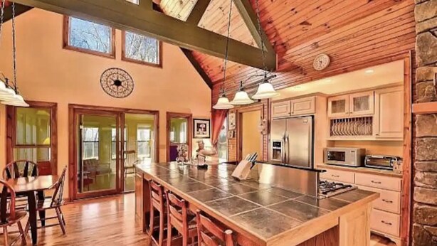 A spacious kitchen with a large island, wooden cabinets, and a stone wall. - ✶Appalachian Mt Cabin, Mt Views, 3BR 3BA, Fiber Wifi, Family, Hiking, Waterfalls (Unicoi)