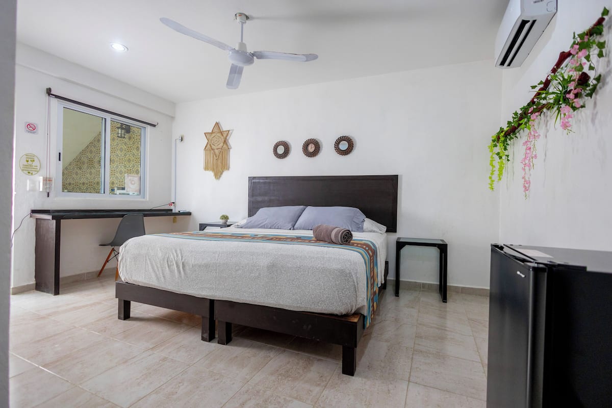 A bedroom with a bed, a desk, a chair, a ceiling fan, and an air conditioner.