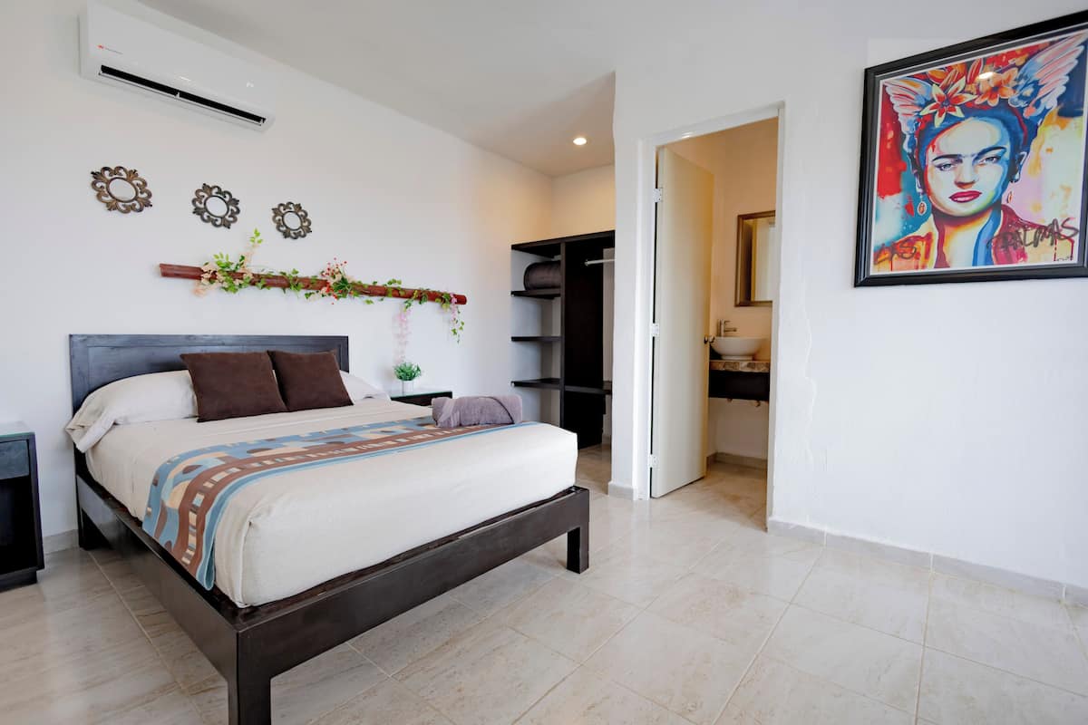A bedroom with a bed, a wardrobe, a bathroom, and a painting on the wall.