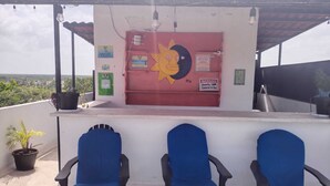 A covered outdoor seating area with three blue chairs, a red wall with various signs, and a view of the landscape. - Hotel Las Palmas Puerto Morelos (Puerto Morelos)