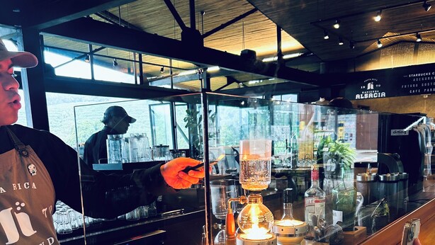 A coffee shop interior with a bar counter, a coffee machine, and a glass display case. - Park View Hotel y Restaurante (Alajuela)