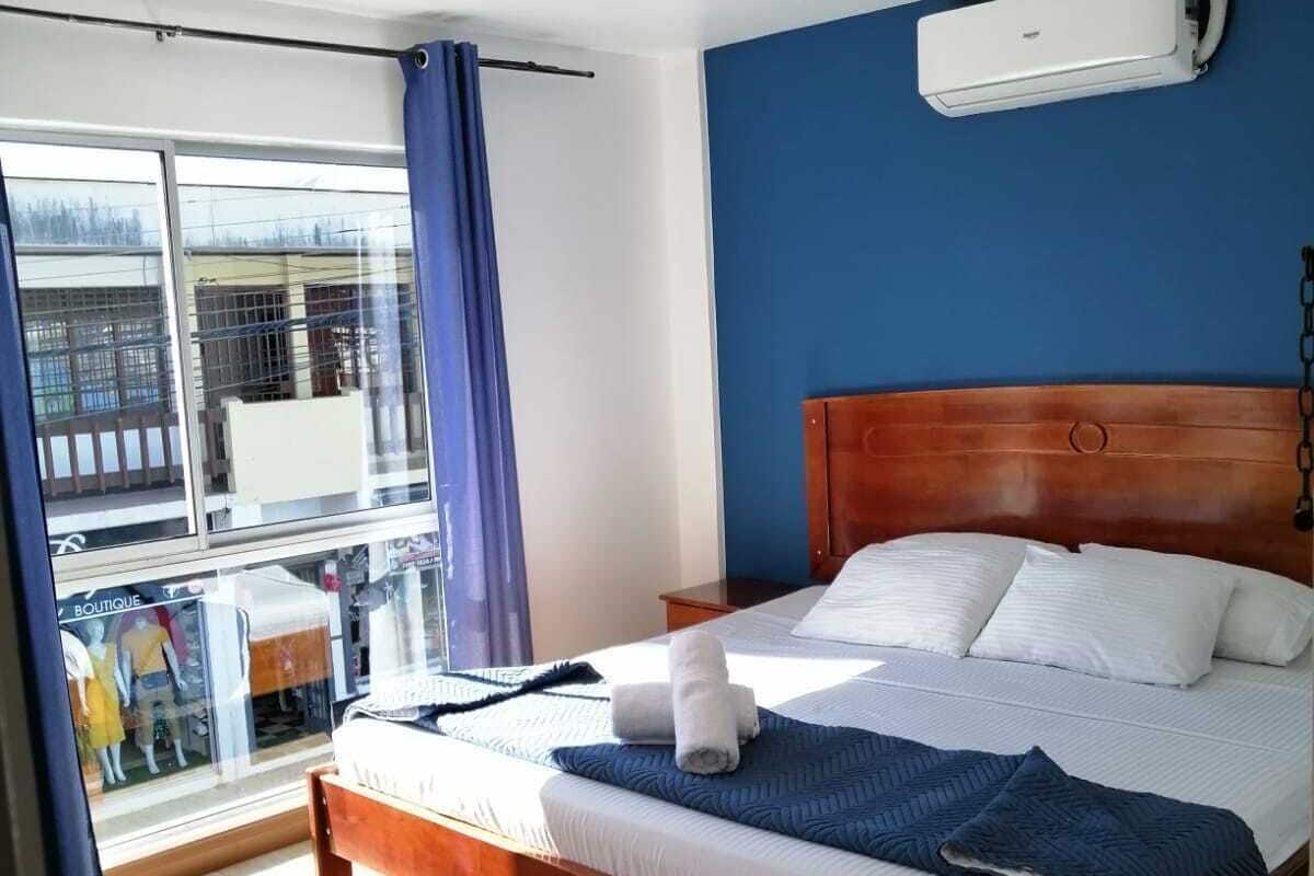 A hotel room with a wooden bed, a large window with a view, and an air conditioning unit on the wall.