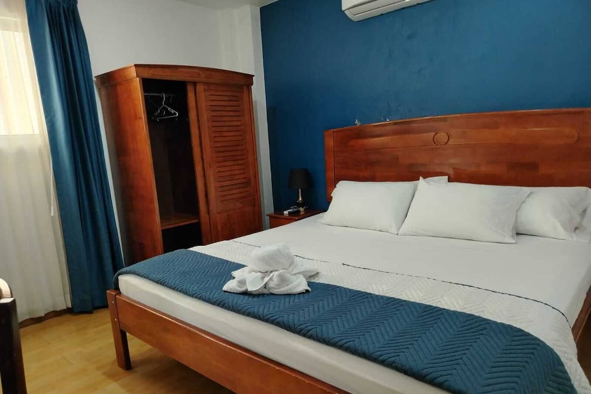 A hotel room with a wooden bed, a wardrobe, a nightstand, and a blue wall.