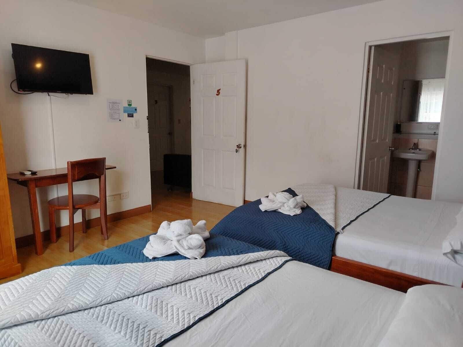 A hotel room with two beds, a desk, a chair, a television, and a bathroom visible through an open door.