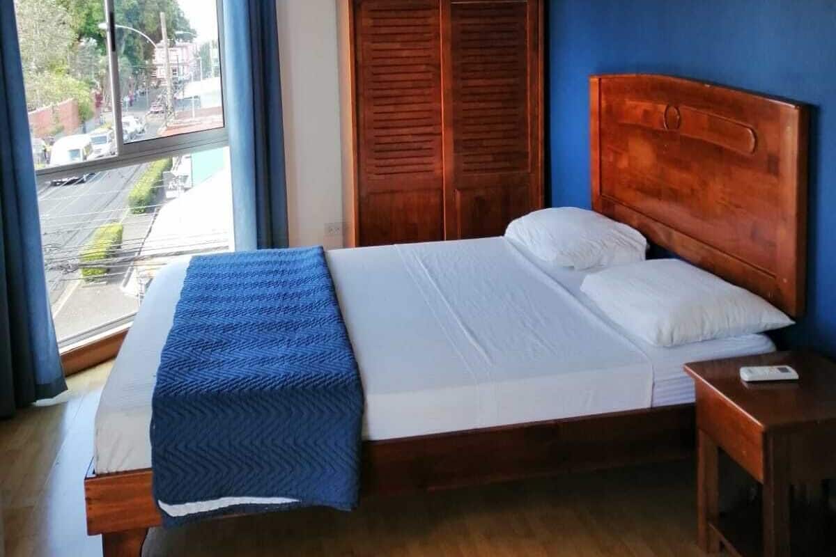 A bedroom with a bed, a wooden wardrobe, a nightstand, and a window with curtains.