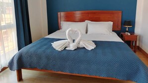 A hotel room with a bed, a wooden headboard, a blue wall, and a window with curtains. - Park View Hotel y Restaurante (Alajuela)