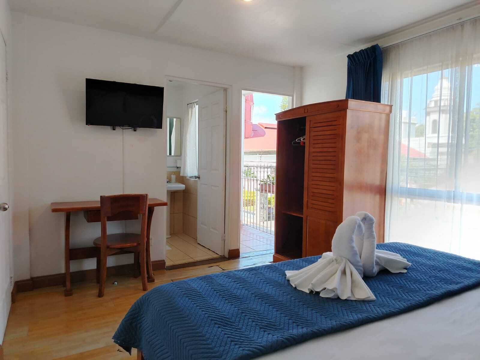 Una habitación de hotel con cama, un escritorio de madera, un televisor montado en la pared y un armario.