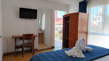 Una habitación de hotel con cama, un escritorio de madera, un televisor montado en la pared y un armario.