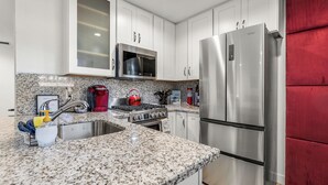 A modern kitchen with white cabinets, stainless steel appliances, granite countertops, and a red accent wall. - Beaver Street Stone Lodge w/AC, Fully Fenced Yard, W/D, 3 Smart TVs, Speedy WiFi (Flagstaff)