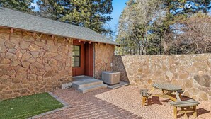 A stone building with a wooden door, a small set of steps leading to the entrance, and a patio area with a table and benches. - Beaver Street Stone Lodge w/AC, Fully Fenced Yard, W/D, 3 Smart TVs, Speedy WiFi (Flagstaff)