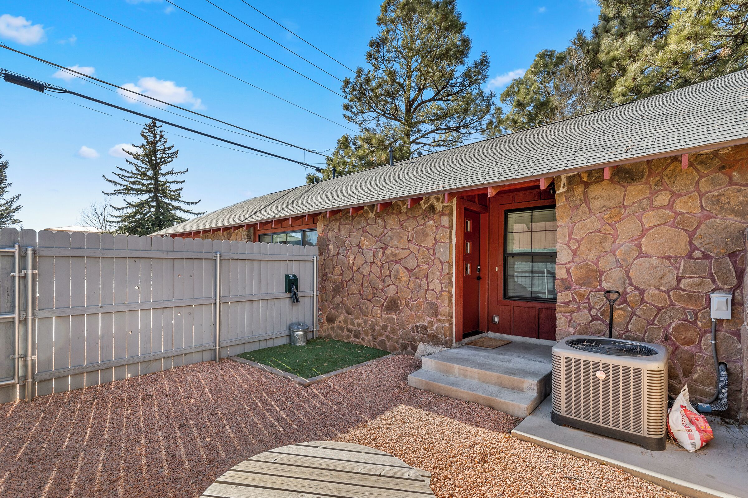 A stone house with a red door, a small front yard with gravel, and a large air conditioning unit.