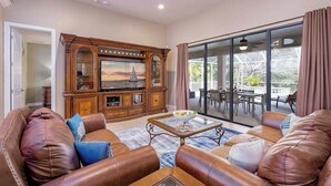 A living room with a leather sofa, a glass coffee table, and a wooden entertainment center with a TV. - Surfside - Bikes and Weight Bench (Cape Coral)