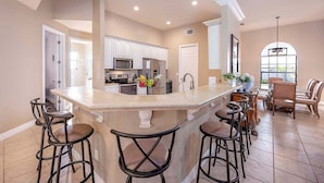 A spacious kitchen with a large island, bar stools, and a dining area with chairs. - Surfside - Bikes and Weight Bench (Cape Coral)