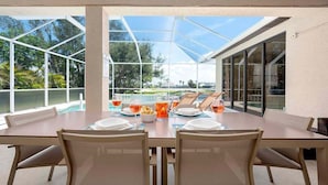 A dining area with a glass-enclosed patio, a table set for four, and a view of the surrounding landscape. - Surfside - Bikes and Weight Bench (Cape Coral)