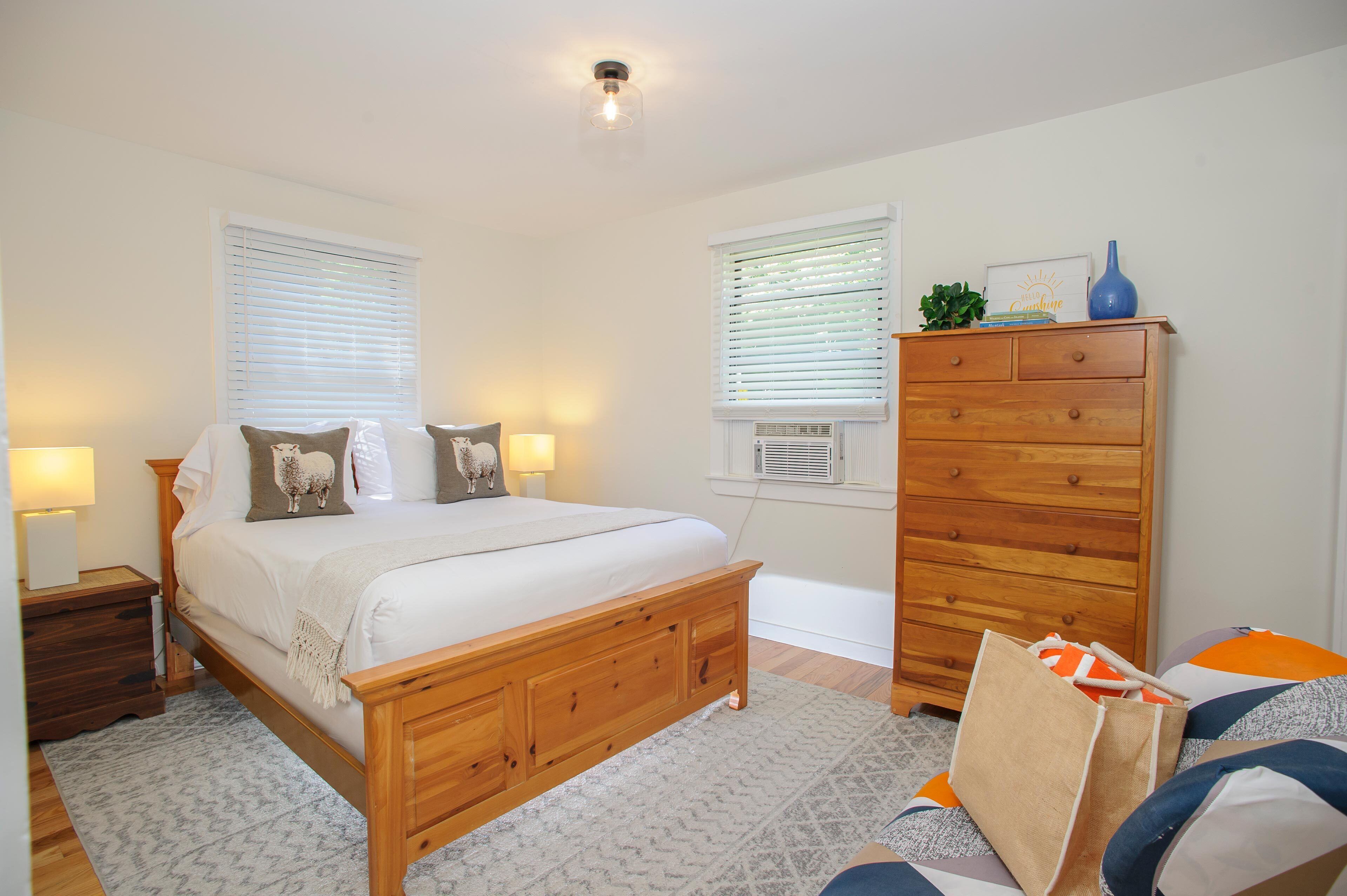 Een slaapkamer met een houten bed, nachtkastjes, een dressoir en een raam met zonwering.