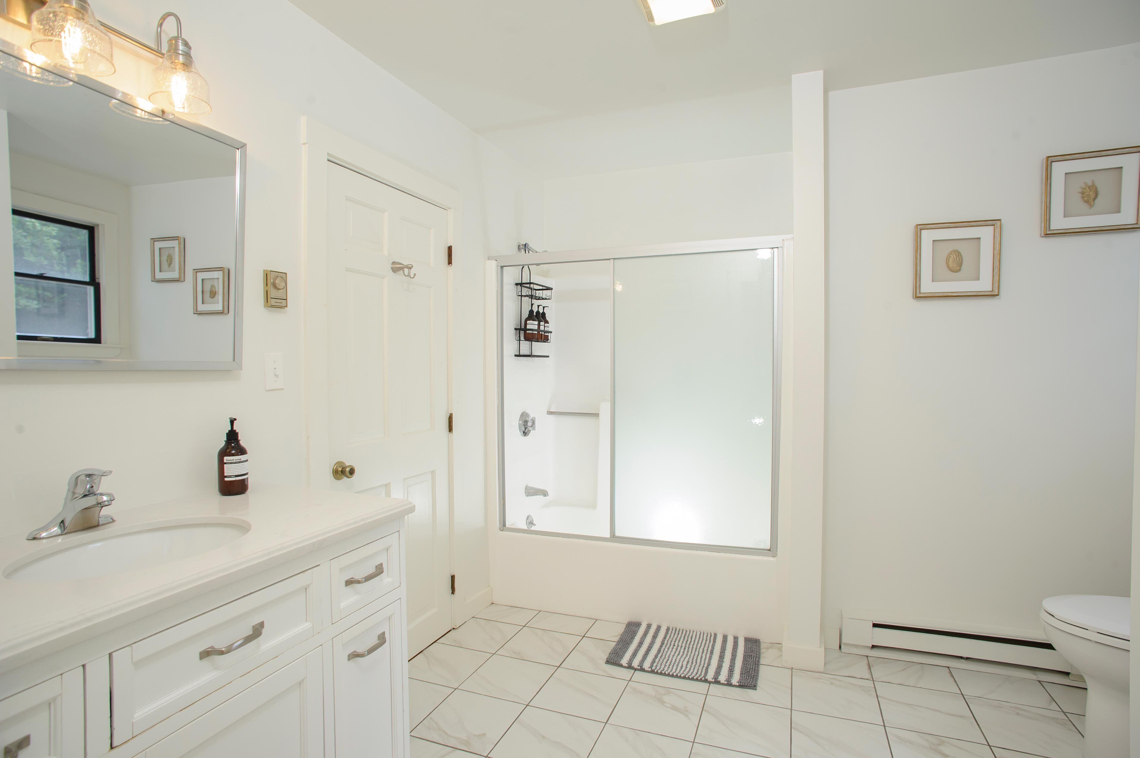 A modern bathroom with a white vanity, a large mirror, a glass shower enclosure, and a toilet.