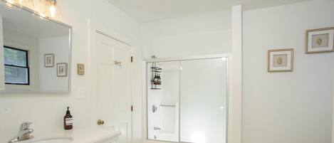 A modern bathroom with a white vanity, a large mirror, a glass shower enclosure, and a toilet.