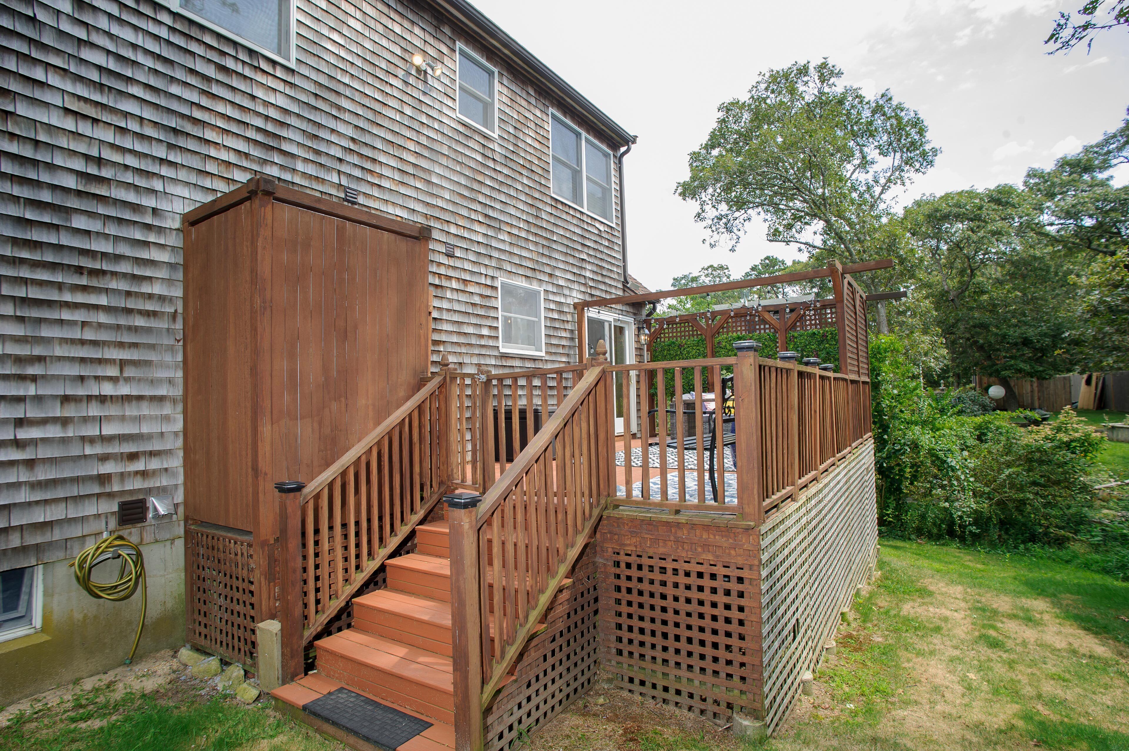 A wooden deck with a staircase leading to a house with a shingled exterior.