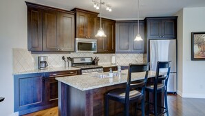 Une cuisine moderne avec des meubles en bois foncé, des appareils en acier inoxydable, un comptoir en granit et un coin bar avec des tabourets.