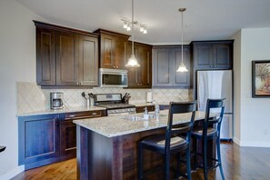 A modern kitchen with dark wood cabinets, stainless steel appliances, a granite countertop, and a bar area with stools.